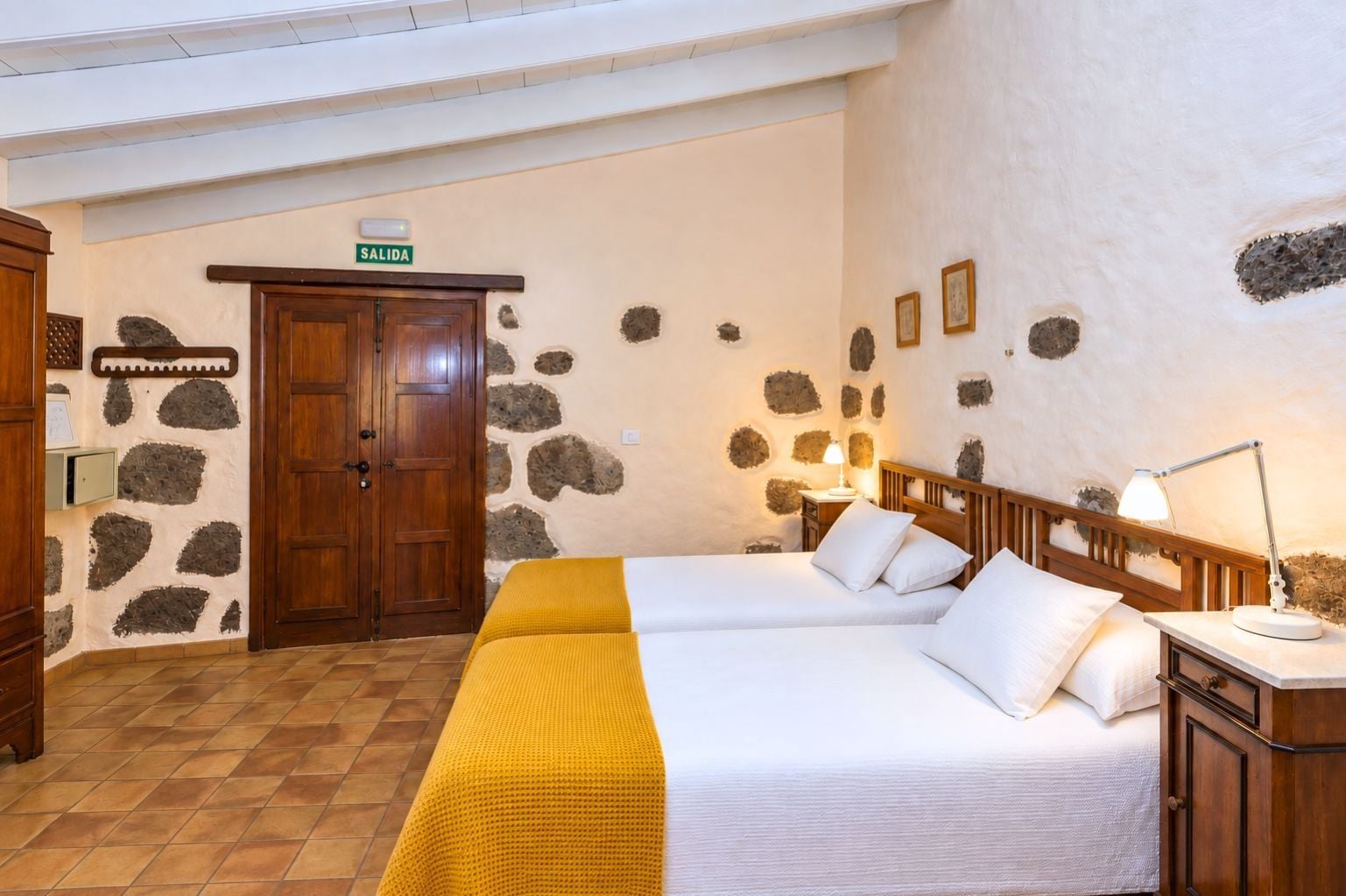 Una habitación con cama, mesita de noche, lámpara, armario y una puerta que indica 'SALIDA'.