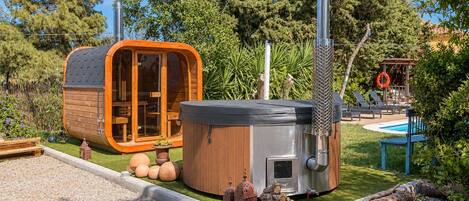 A hot tub and a wooden structure with a glass door, surrounded by a pool and greenery.