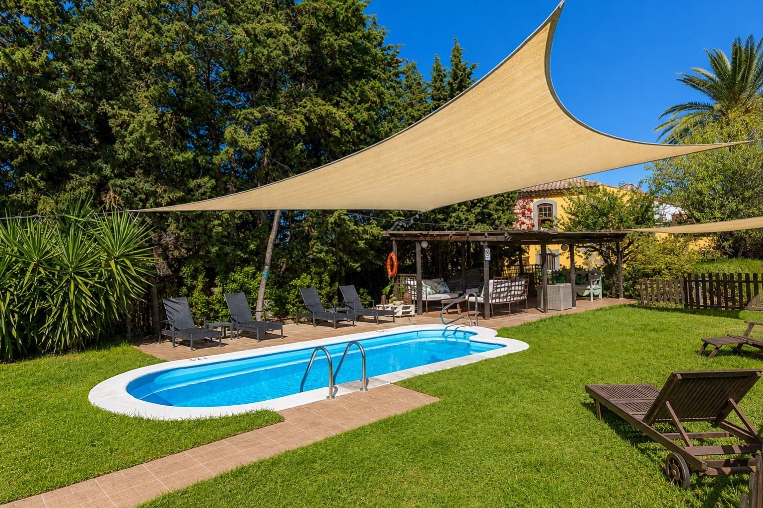 A swimming pool with a shaded area, lounge chairs, and a covered patio.
