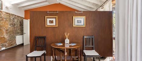 A dining area with a wooden table and chairs, framed pictures on the wall, and a stone wall.