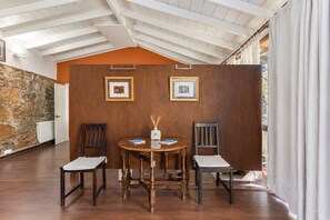 A dining area with a wooden table and chairs, framed pictures on the wall, and a stone wall. - Guestready - Hotel Rural Las Calas (Vega de San Mateo)