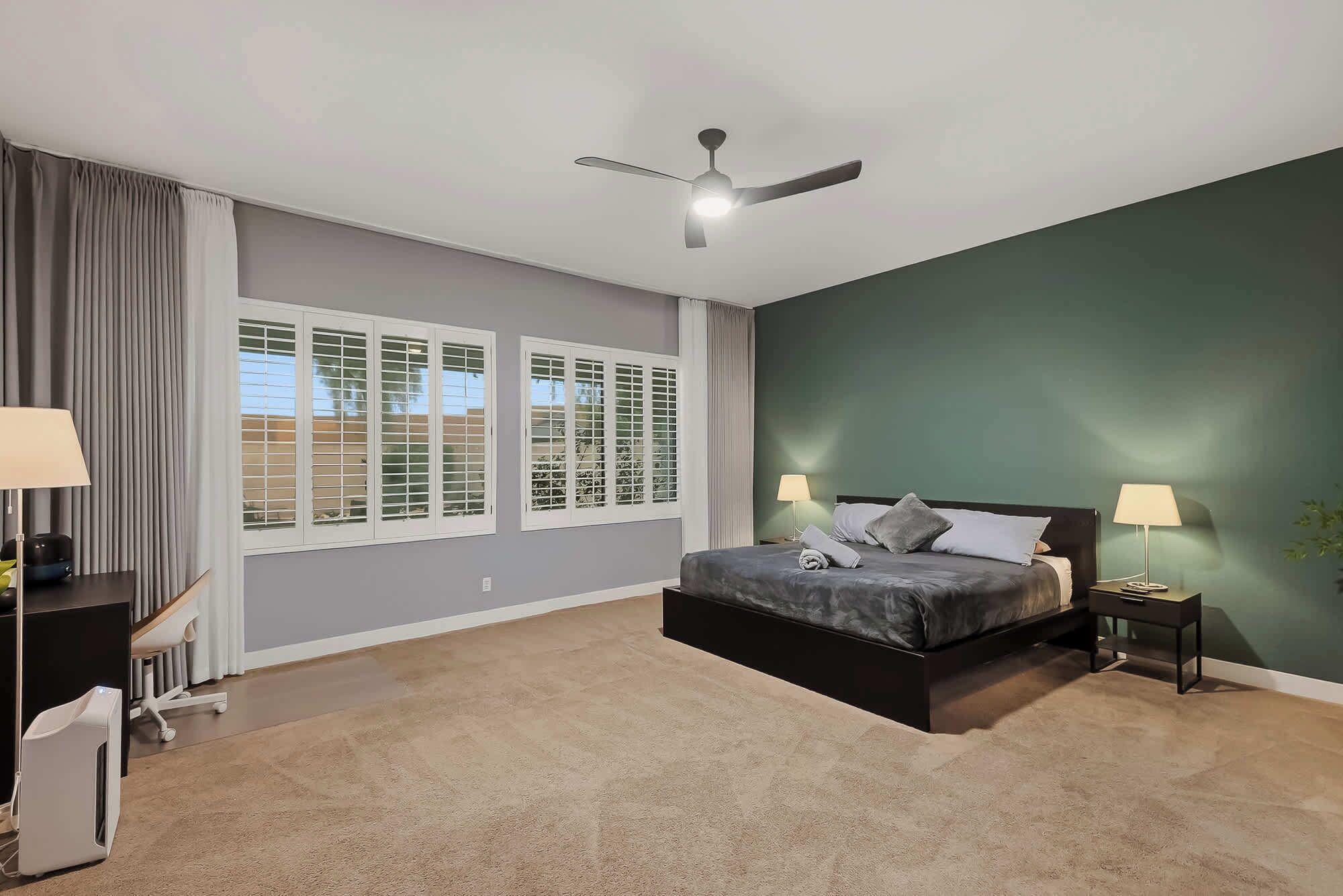 A bedroom with a bed, two bedside tables, a ceiling fan, and a window with blinds.