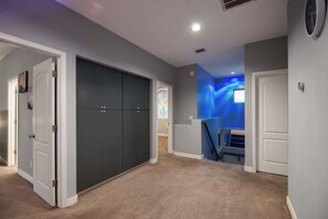 A hallway with a carpeted floor, a dark closet, and a staircase leading to a room with a blue wall. - Relaxing 5BR Tempe Home family pool moder home (Tempe)