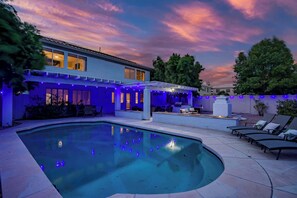 A swimming pool with a patio area, a covered seating space, and a house with blue ambient lighting. - Relaxing 5BR Tempe Home family pool moder home (Tempe)