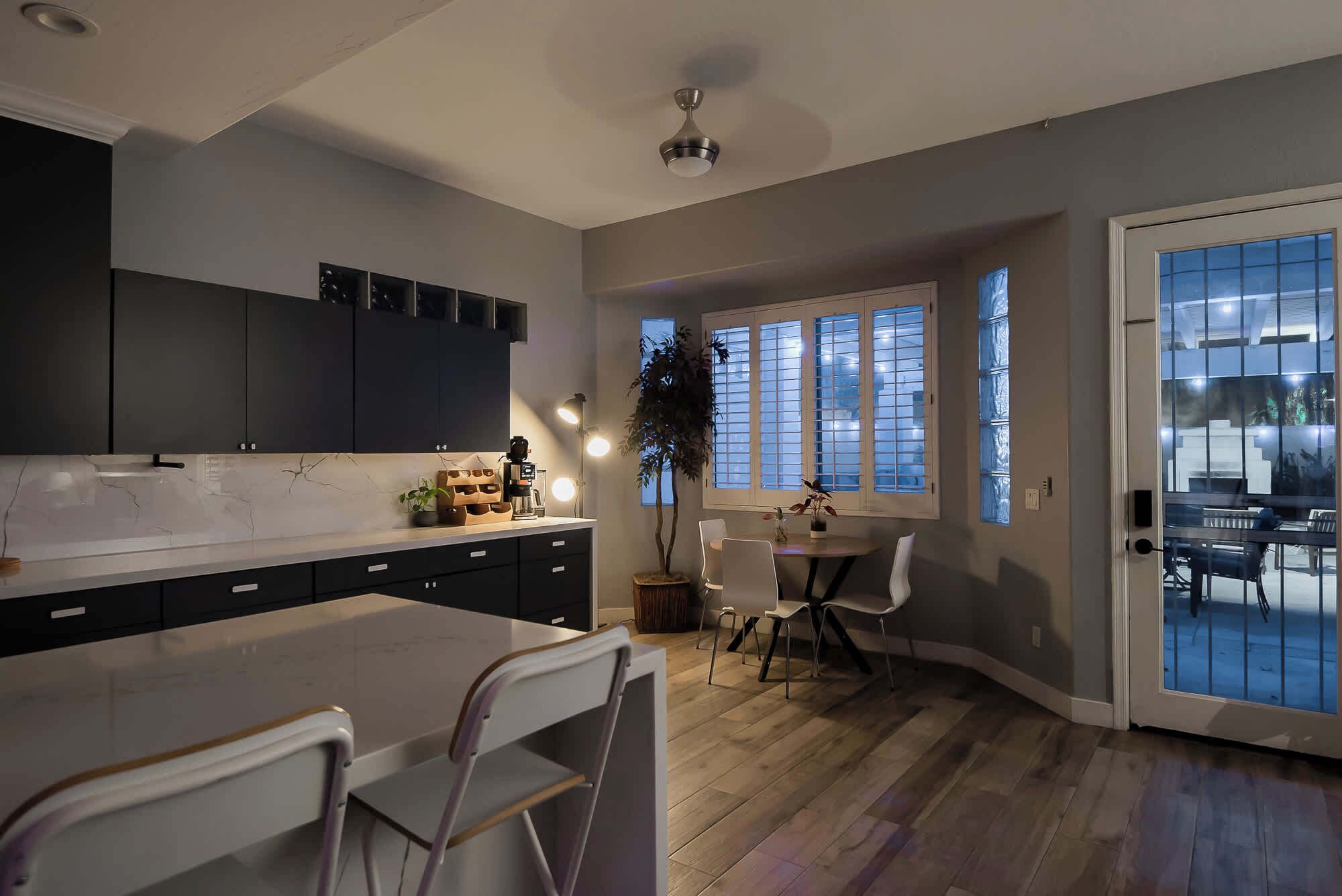 A modern kitchen with dark cabinets, a marble countertop, and a dining area with a table and chairs.
