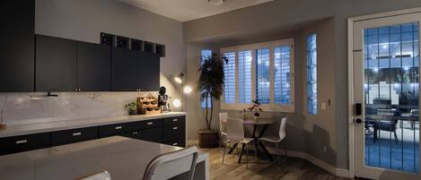 A modern kitchen with dark cabinets, a marble countertop, and a dining area with a table and chairs.