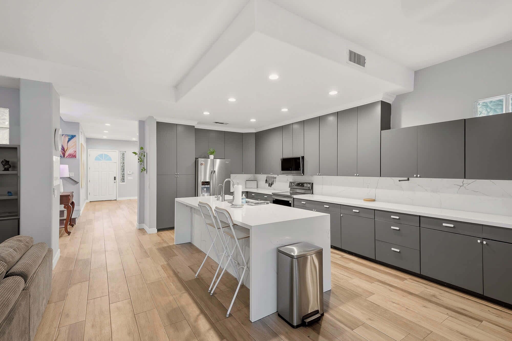 A modern kitchen with grey cabinets, a white countertop, and a stainless steel trash bin.