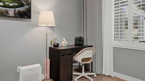Een hoekzaak met een bureau, stoel, lamp en een raam met zonwering.