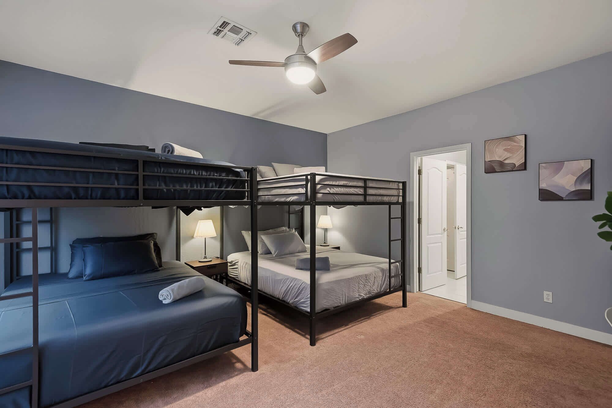 A room with bunk beds, a ceiling fan, a door, and two bedside lamps.