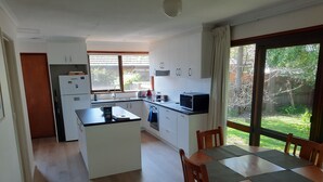 Ett modernt kök med vita skåp, en köksö och en matplats med bord och stolar.