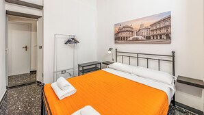 A hotel room with a bed, a nightstand, a lamp, a coat rack, and a painting of a historic building. - Da Stefano Historical Center 5 min to Aquarium (Genoa)