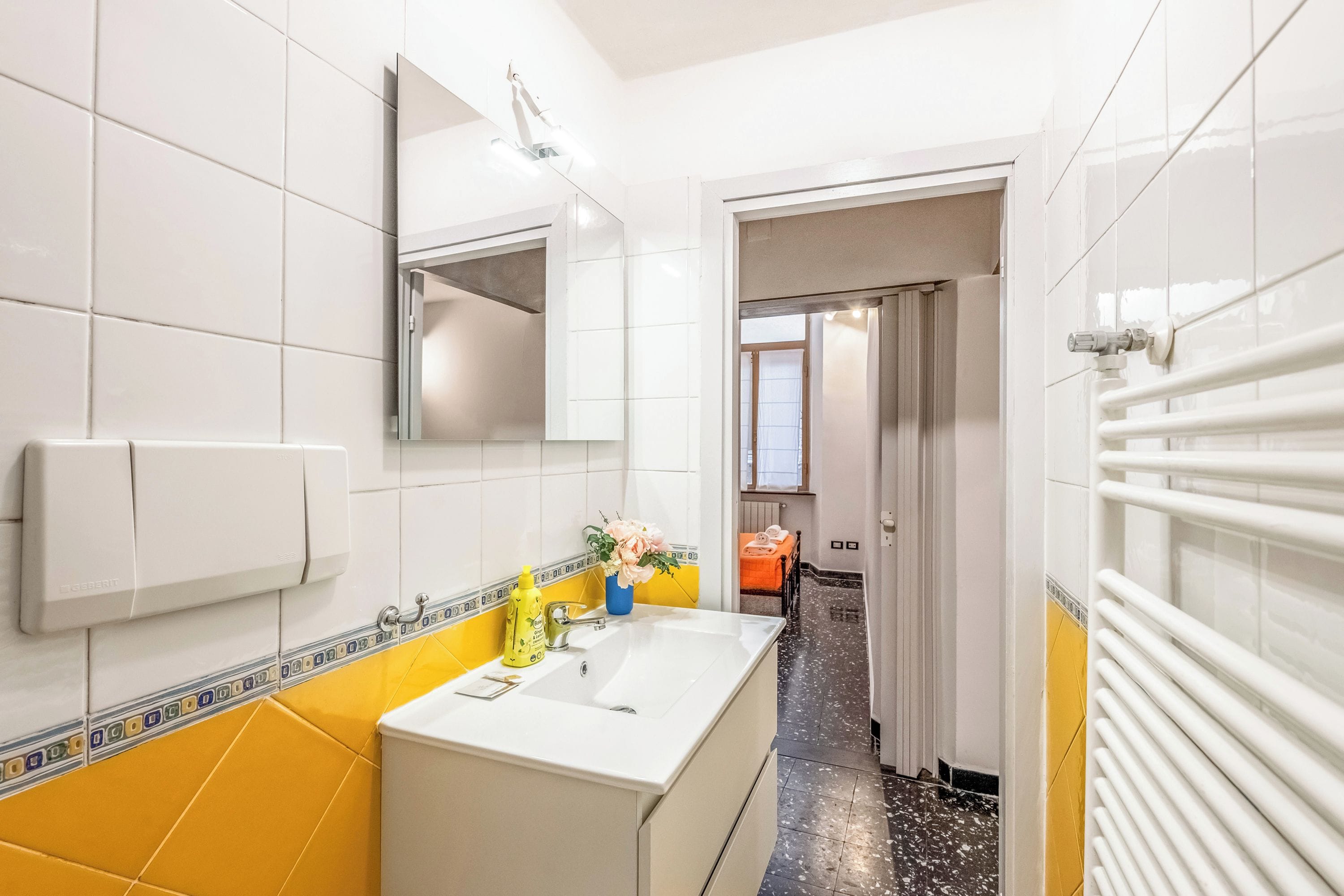 Une salle de bain avec un lavabo blanc, des murs carrelés de jaune et de blanc, un miroir et un radiateur.