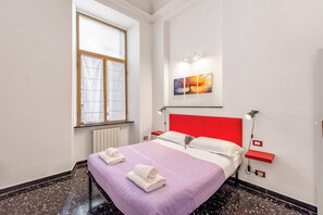 A neatly arranged bedroom with a bed, a window, a radiator, a red headboard, wall-mounted artwork, bedside lamps, and a red shelf. - Da Stefano Historical Center 5 min to Aquarium (Genoa)