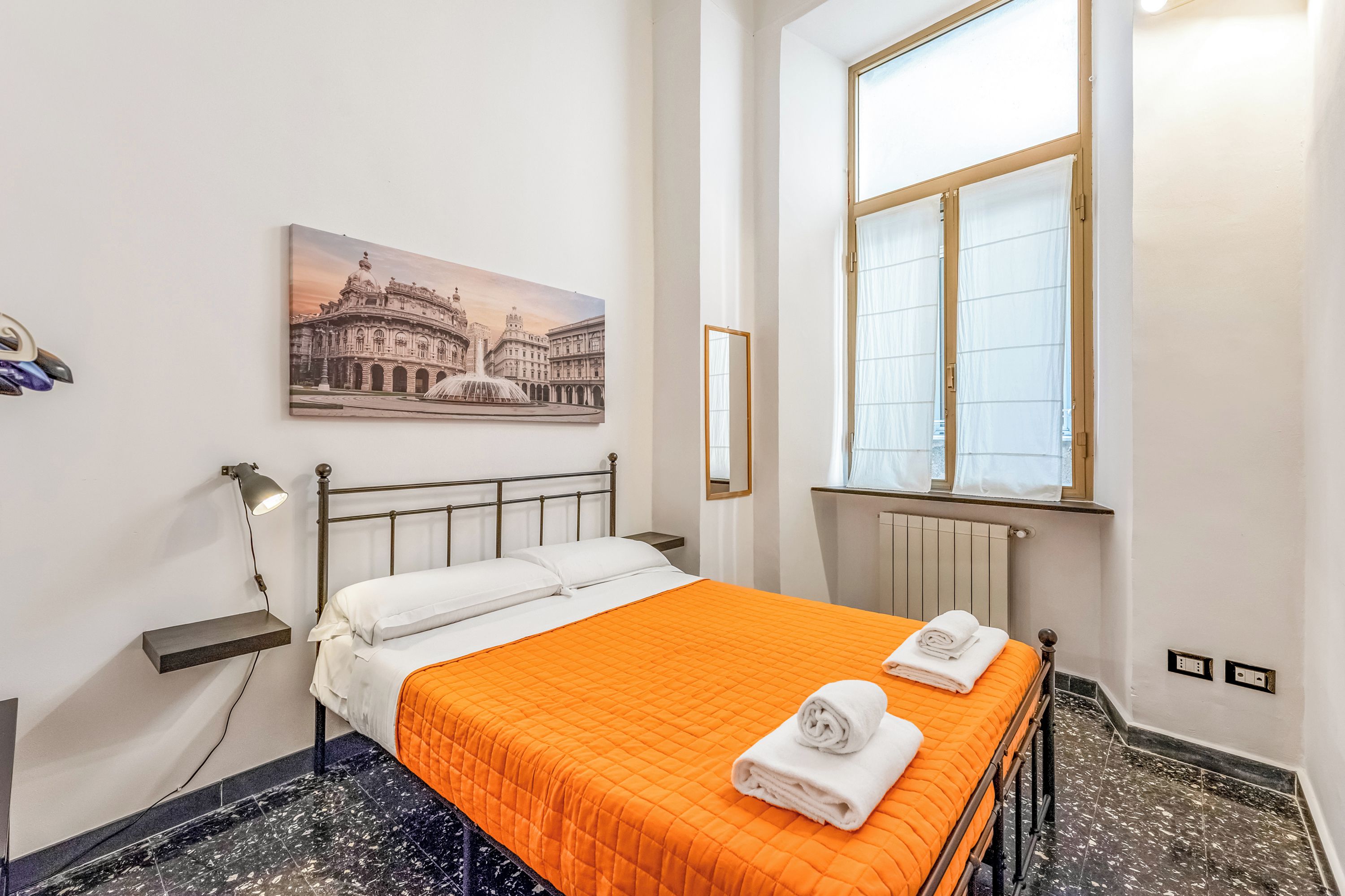 Una habitación de hotel con una cama, un cuadro de un edificio histórico, una ventana con cortinas y un radiador.