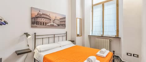Una habitación de hotel con una cama, un cuadro de un edificio histórico, una ventana con cortinas y un radiador.