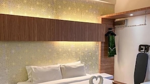 Habitación de hotel con cama, almohadas, una disposición de toallas con forma de corazón, bata y aire acondicionado de pared.