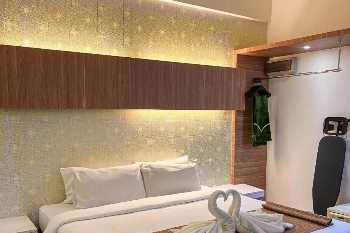 A hotel room with a bed, pillows, a heart-shaped towel arrangement, a robe, and a wall-mounted air conditioning unit.