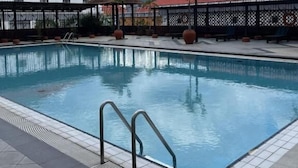 Una piscina con borde de baldosas, barandillas metálicas y un área cercada, con un edificio al fondo.