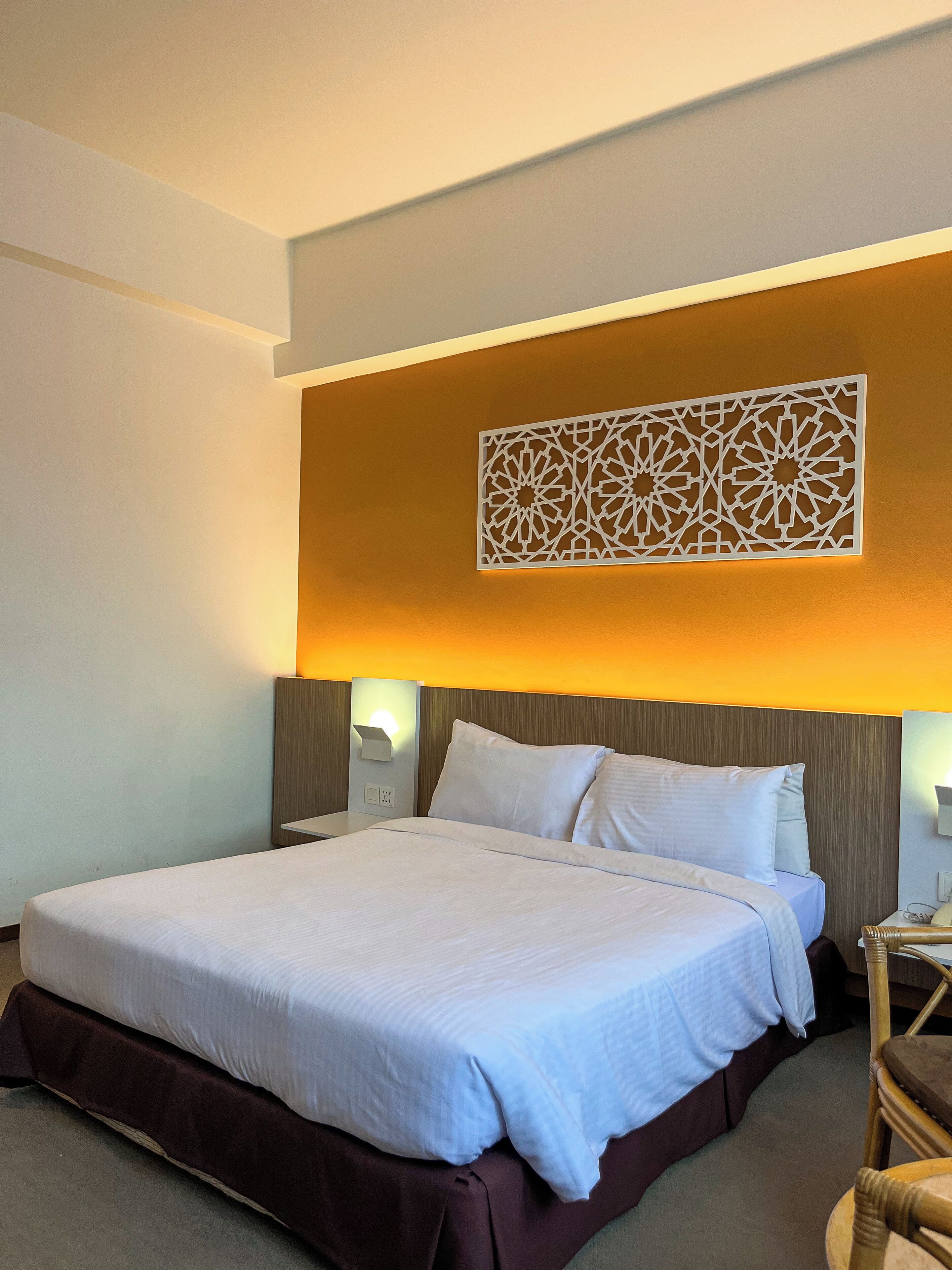 Habitación de hotel con una cama grande, dos mesitas de noche, un panel decorativo y una mesita con lámpara.
