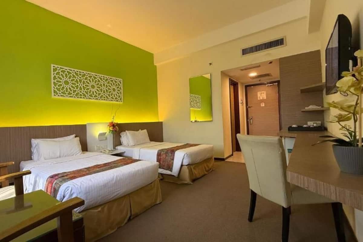 A hotel room with two beds, a desk, a chair, a TV, and a potted plant.