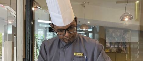 Un chef cocina en una cocina moderna con estufa a gas, utensilios de cocina de acero inoxidable y un gafete.