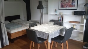 A compact room with a bed, a table with chairs, a bookshelf, and a desk with a lamp. - House Begonia Room No. 5 (Siegsdorf)