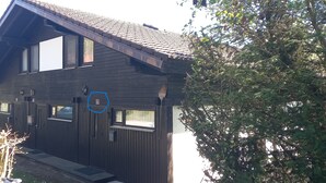 A two-story wooden house with a sloped roof, multiple windows, and a visible door. - Vacation apartment type C/Salzburg (Siegsdorf)
