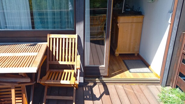 A wooden deck with a table and chairs, a sliding glass door leading to a room, and a wooden cabinet. - Vacation apartment type C/Salzburg (Siegsdorf)