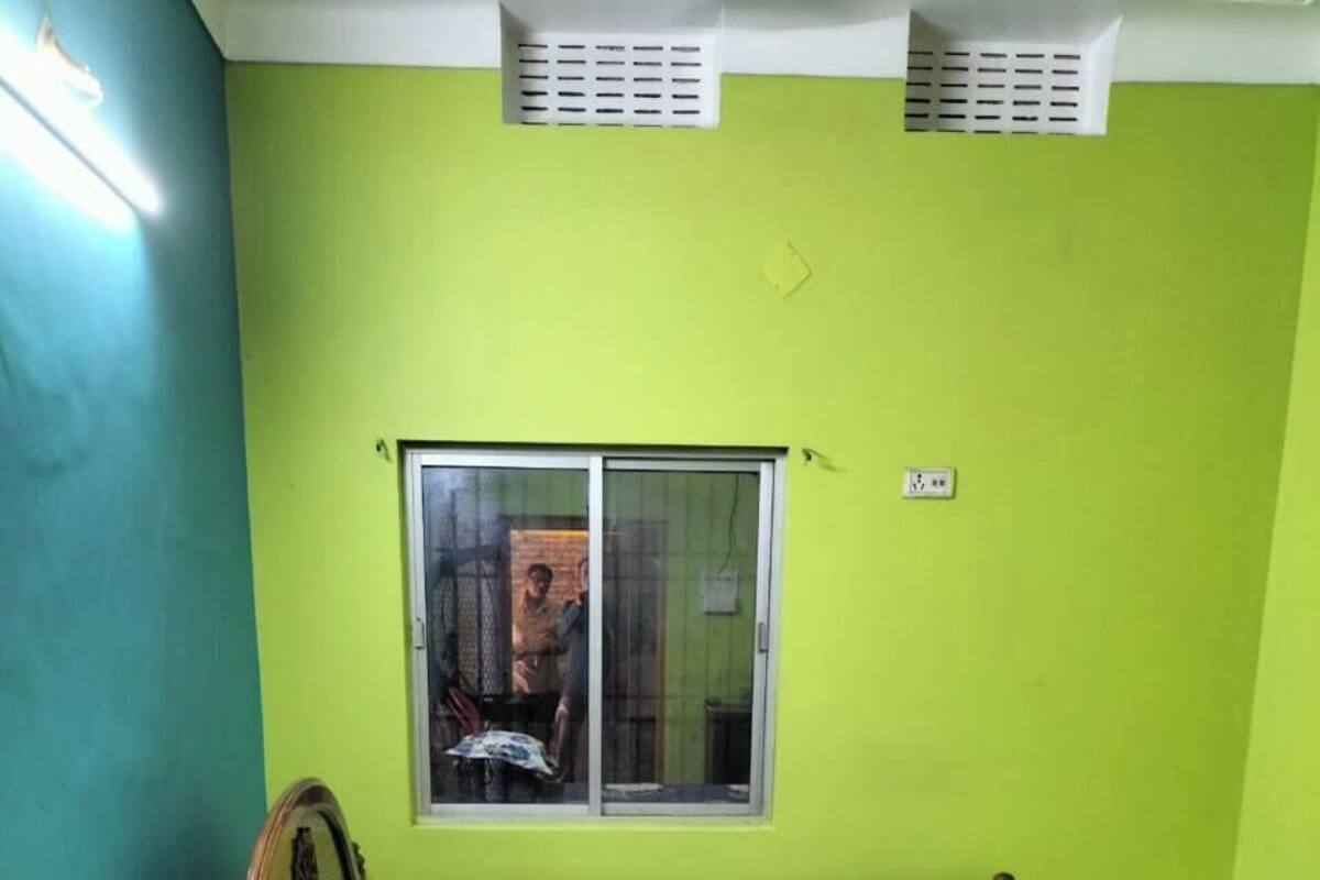 Una habitación con cama, ventana, una silla roja y pared verde.