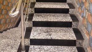 Una escalera con barandilla de metal, pared de piedra y pared amarilla.