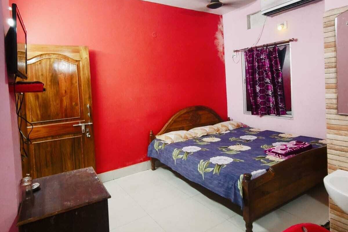 Un dormitorio con una cama de madera, una pared roja, un ventilador de techo, aire acondicionado y una ventana con cortinas.