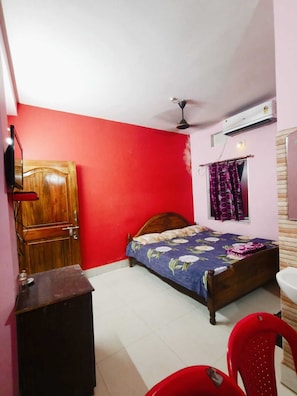 A bedroom with a wooden bed, a red wall, a ceiling fan, an air conditioner, and a window with curtains.