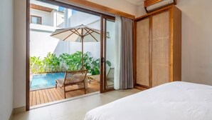 A hotel room with a bed, a sliding glass door to a pool area, a ceiling fan, and a woven partition. - Cassandra Villas - Your Bali Escape (Denpasar)
