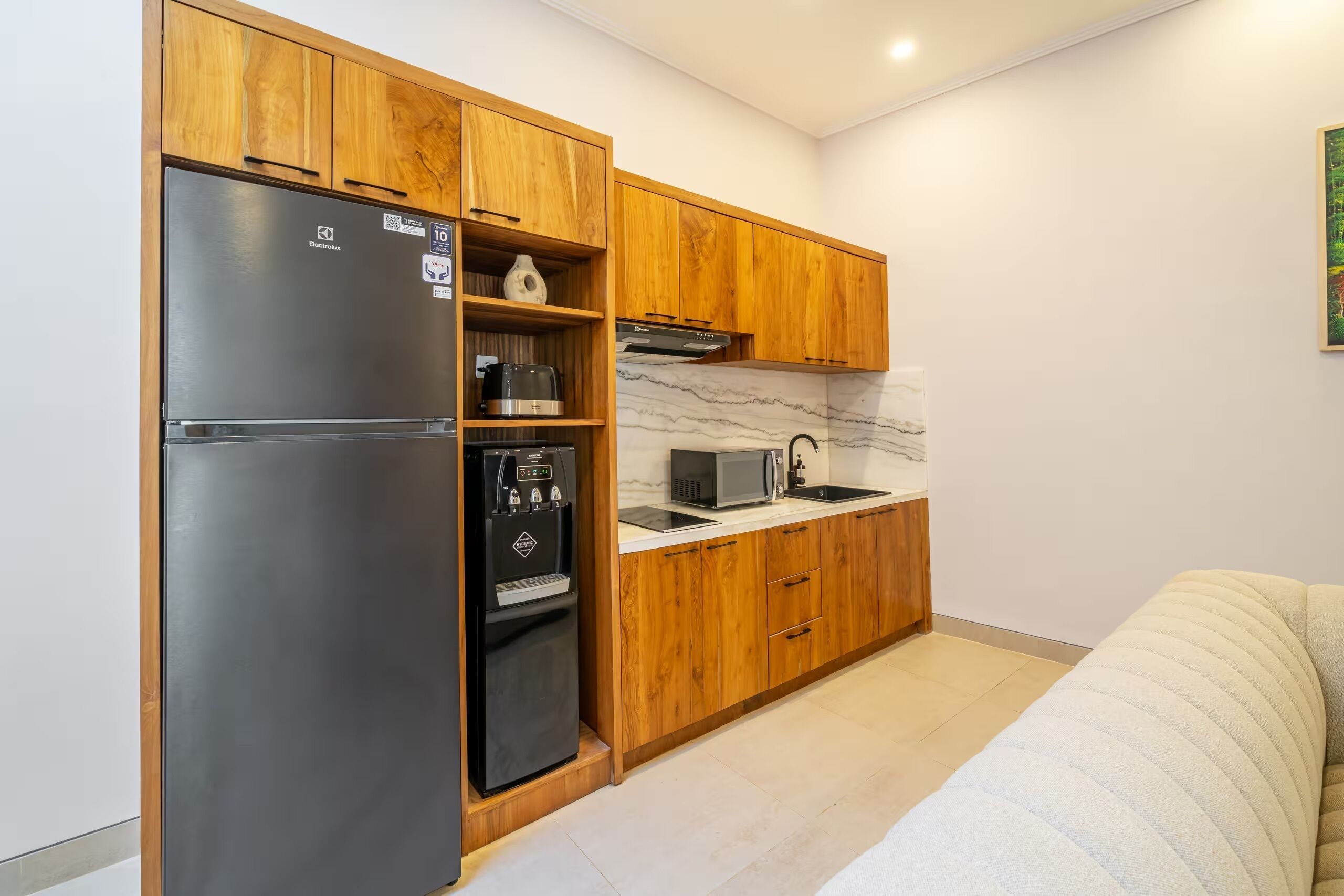 A compact kitchen with wooden cabinets, a stainless steel refrigerator, a microwave, and a water dispenser.