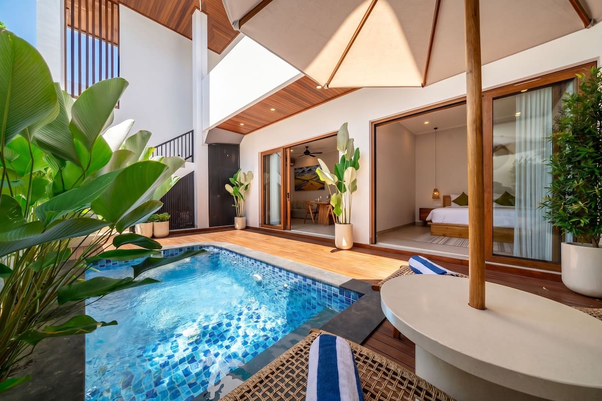 Un área de piscina moderna con una piscina azul cristalina, terraza de madera y plantas en macetas.