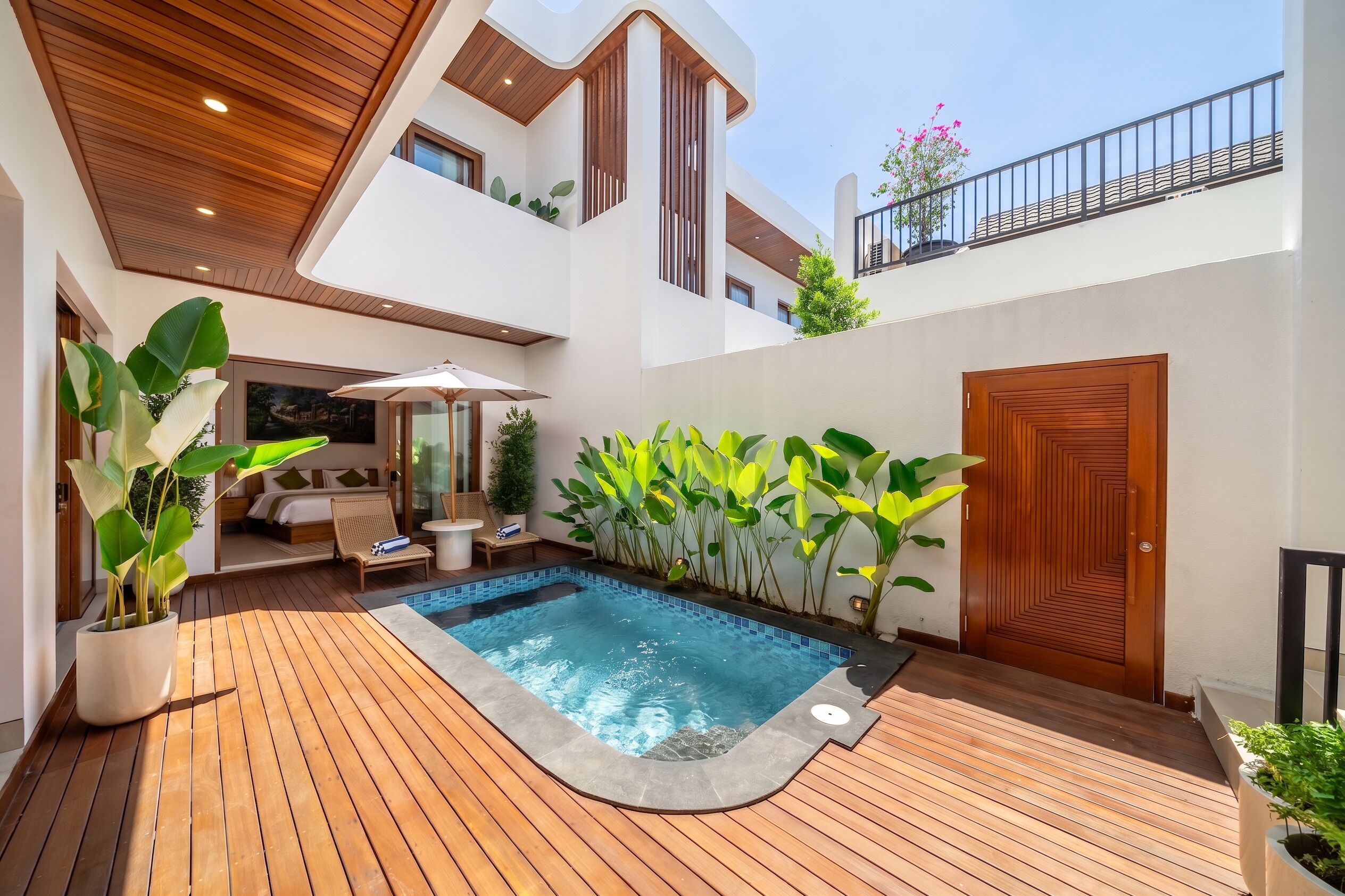 Un área de piscina moderna al aire libre con terraza de madera, un jacuzzi y una silla de descanso.
