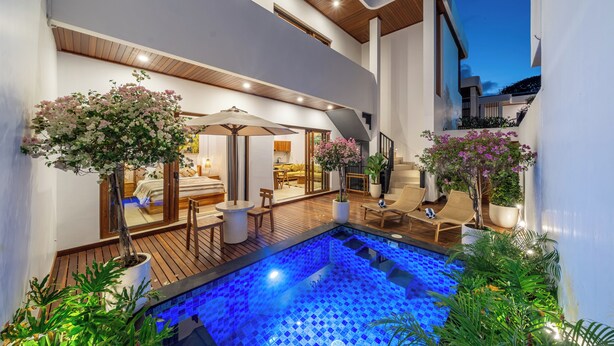 A modern outdoor pool area with a wooden deck, lounge chairs, and potted plants. - Cassandra Villas - Your Bali Escape (Denpasar)