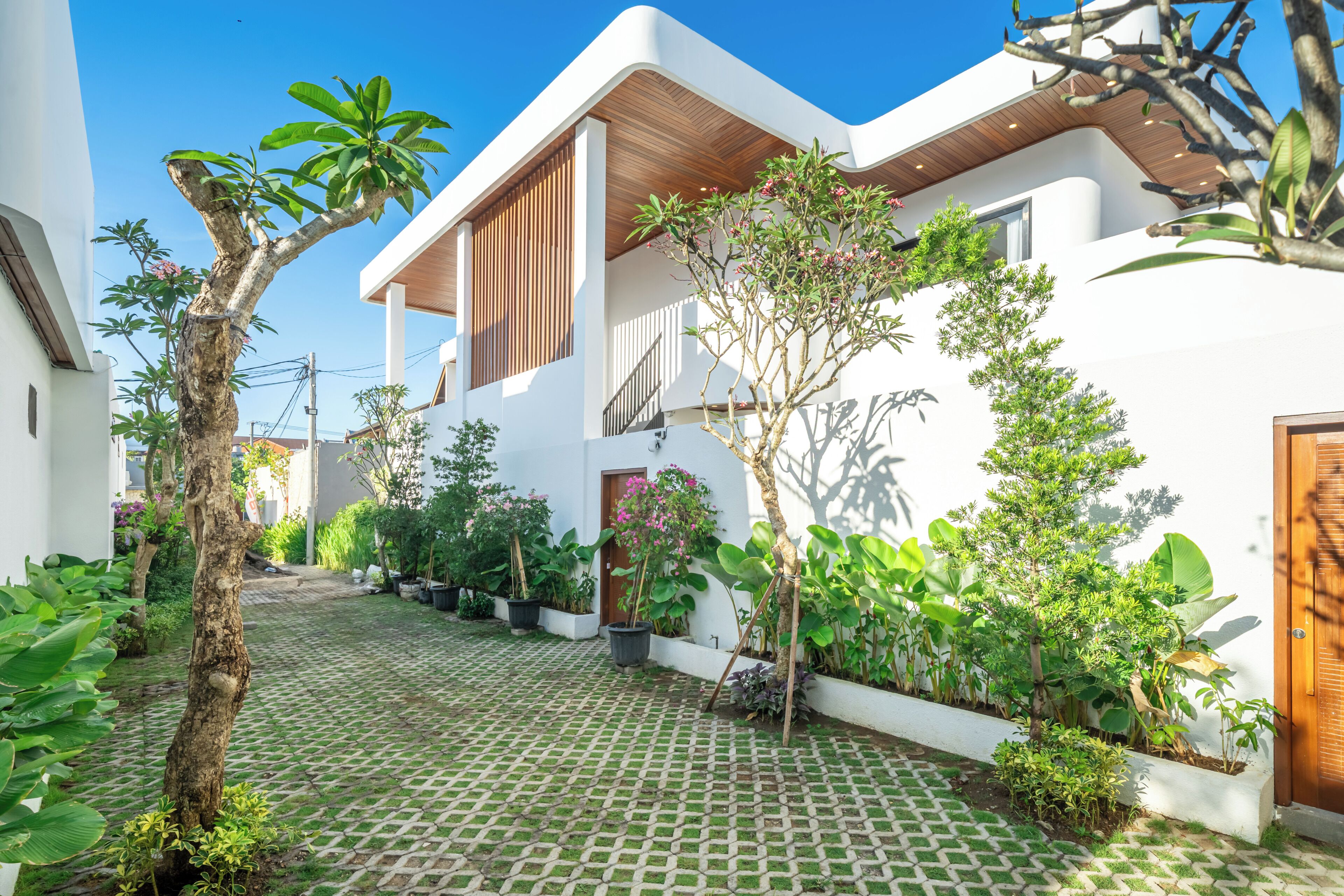 A modern house with a paved courtyard, potted plants, and a wooden door.