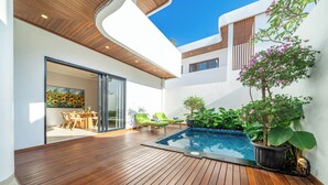 A modern outdoor area with a wooden deck, a swimming pool, and a dining area with green chairs. - Cassandra Villas - Your Bali Escape (Denpasar)