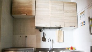 A kitchen with wooden cabinets, a stove, a sink, and a hanging pot rack. - Casa vacanze Ureshii a San Foca (San Foca)
