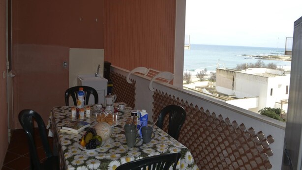 A balcony with a table set for breakfast, a view of the sea, and a white wall with a window. - Casa vacanze Ureshii a San Foca (San Foca)