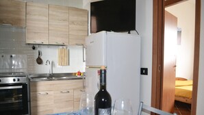 A kitchen with a dining area, a TV mounted above the fridge, and a bed visible through an open door. - Casa vacanze Ureshii a San Foca (San Foca)