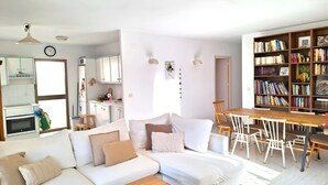 Un espace de vie moderne comprenant un canapé, une table basse, une table à manger, des chaises, une bibliothèque et un coin cuisine.