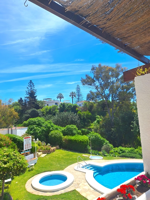 Ein Garten mit zwei Pools, einer überdachten Terrasse und umgebender Bepflanzung.