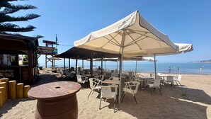 Un café situé en bord de mer, avec une terrasse, un tonneau en bois et une vue sur l’océan.