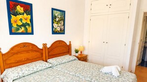 Een slaapkamer met een houten hoofdeinde, twee bedden met beddengoed met een patroon, een nachtkastje met een lamp en een witte inloopkast.