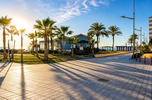 A paved walkway with palm trees, a building with a blue facade, and a clear sky. - Lentiscares 213 Beach & Pool – Torrox Costa (Torrox Costa)