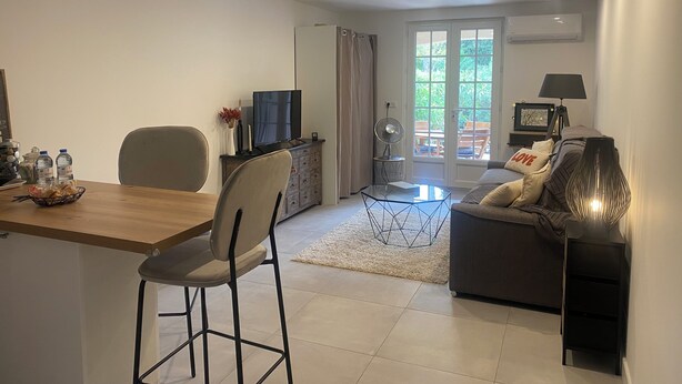 A modern living room with a dining area, a sofa, a TV, and a door leading to an outdoor patio. - Charming studio with garden in St-Raphaël (Saint-Raphaël)