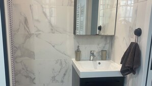 A modern bathroom with a marble backsplash, a white sink, a dark cabinet, a towel rack, and a small potted plant. - Charming studio with garden in St-Raphaël (Saint-Raphaël)