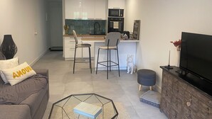 A modern living room with a sofa, a glass coffee table, a TV, and a kitchen area with a microwave and a sink. - Charming studio with garden in St-Raphaël (Saint-Raphaël)